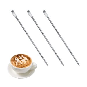 Tre latte art-pennor bredvid en kopp kaffe med bladmotiv i skummet.