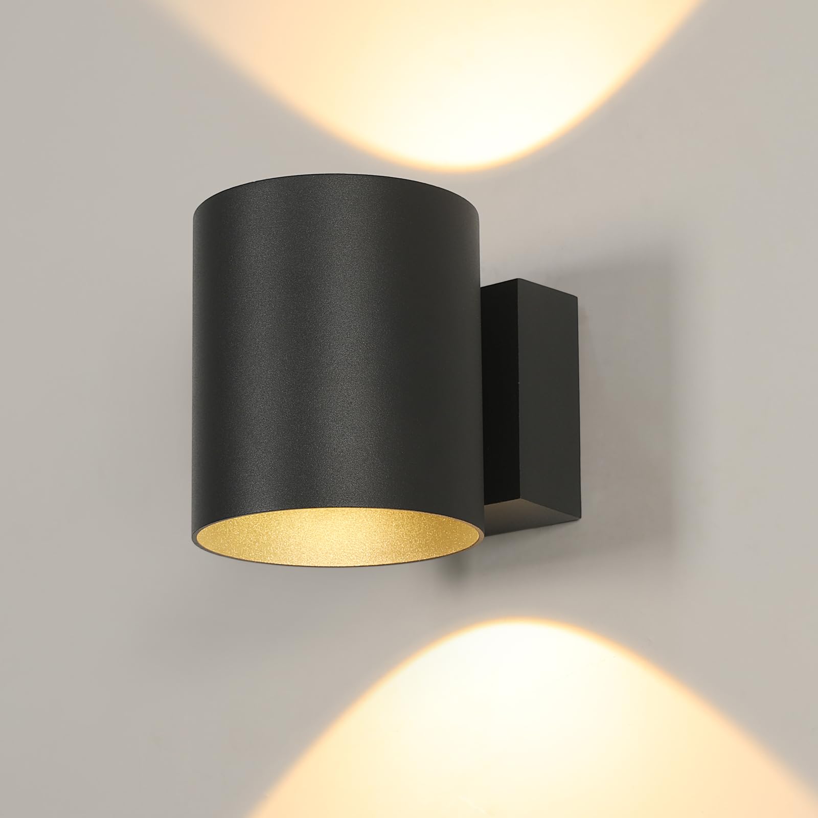 Svart vägglampa med cylindrisk kupa som lyser uppåt och nedåt mot en vägg.