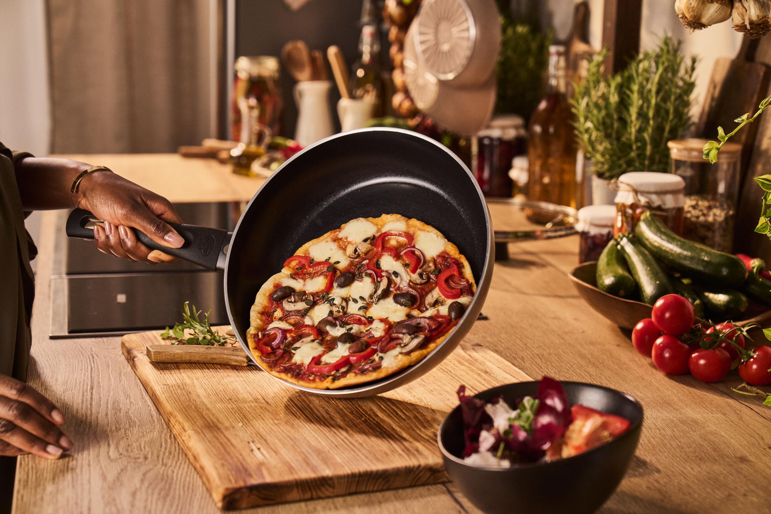 Stekpanna med en färdiggräddad pizza hålls upp över en köksbänk.