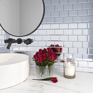 Vitt badrum med silverfärgat kakelmönster, runt spegel, blommor och ljus.