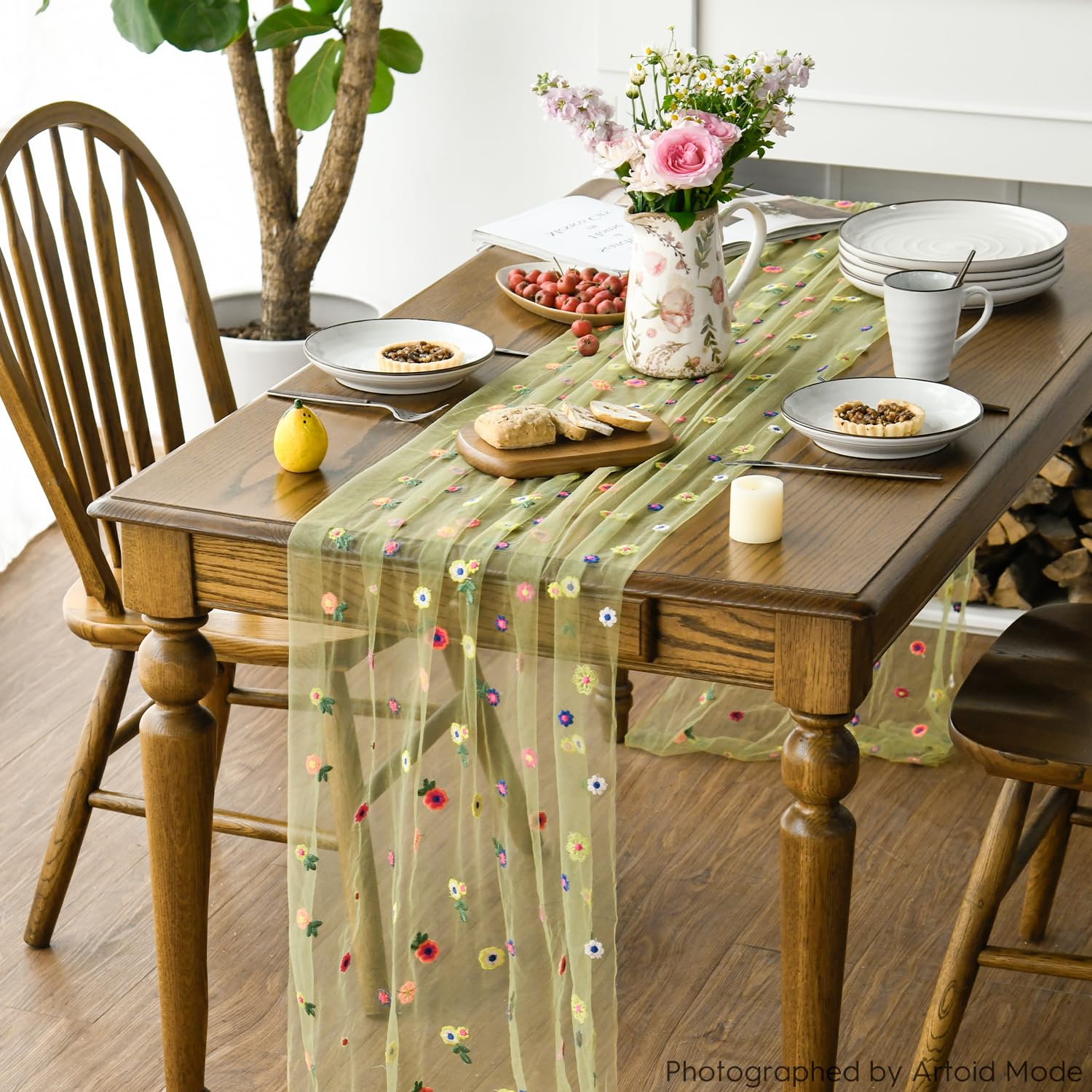 Grön tyllöpare med färgglada broderade blommor på ett dukat träbord.