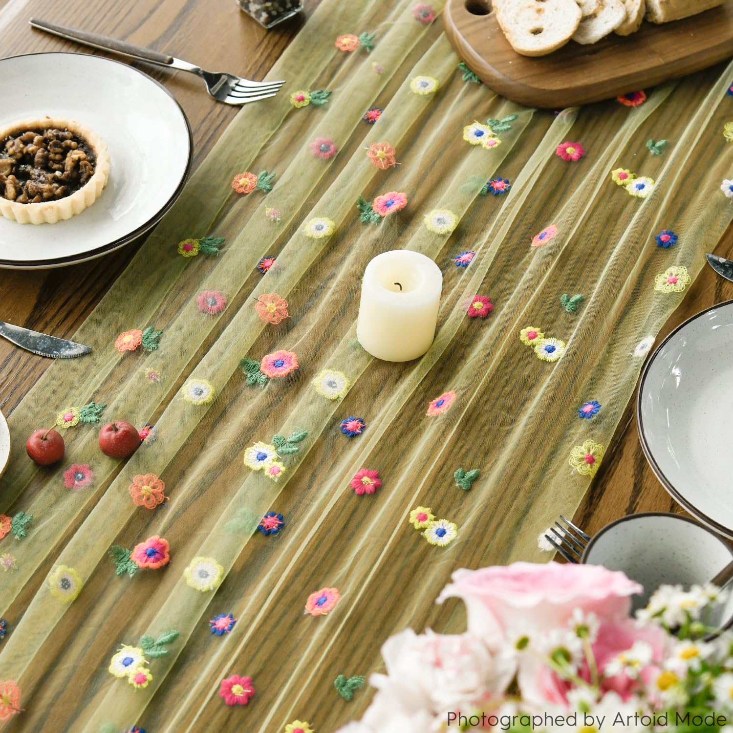Grön bordslöpare med färgglada broderade blommor på dukat träbord.
