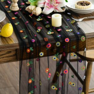 Svart bordslöpare med färgglada blommor och broderade detaljer över ett dukat träbord.