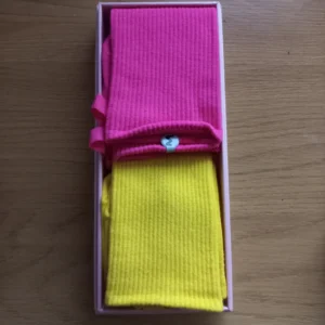 Två par räfflade strumpor i rosa och gult, placerade i en ask.