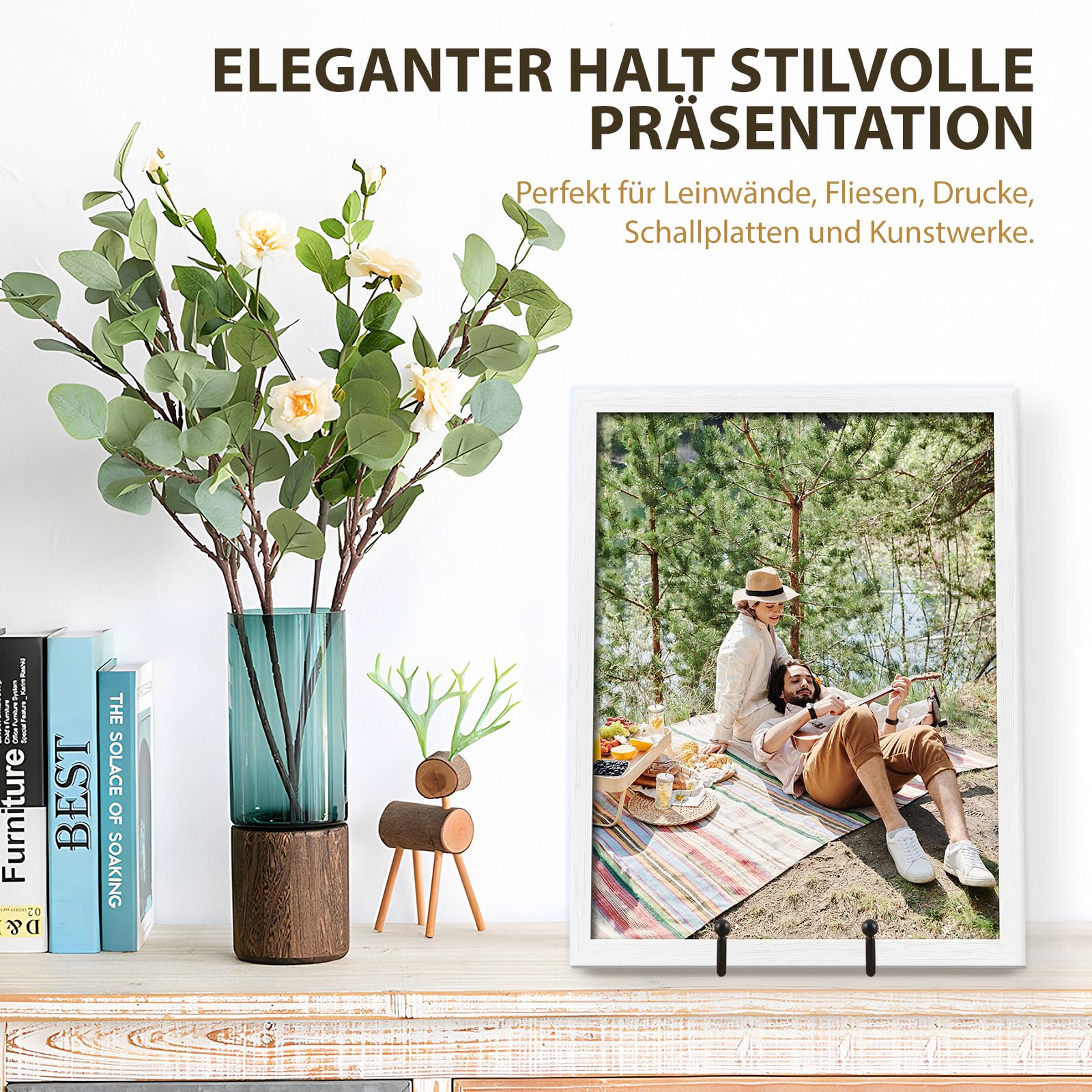 Svart metallställ håller en inramad tavla på en hylla bredvid en vas och böcker.