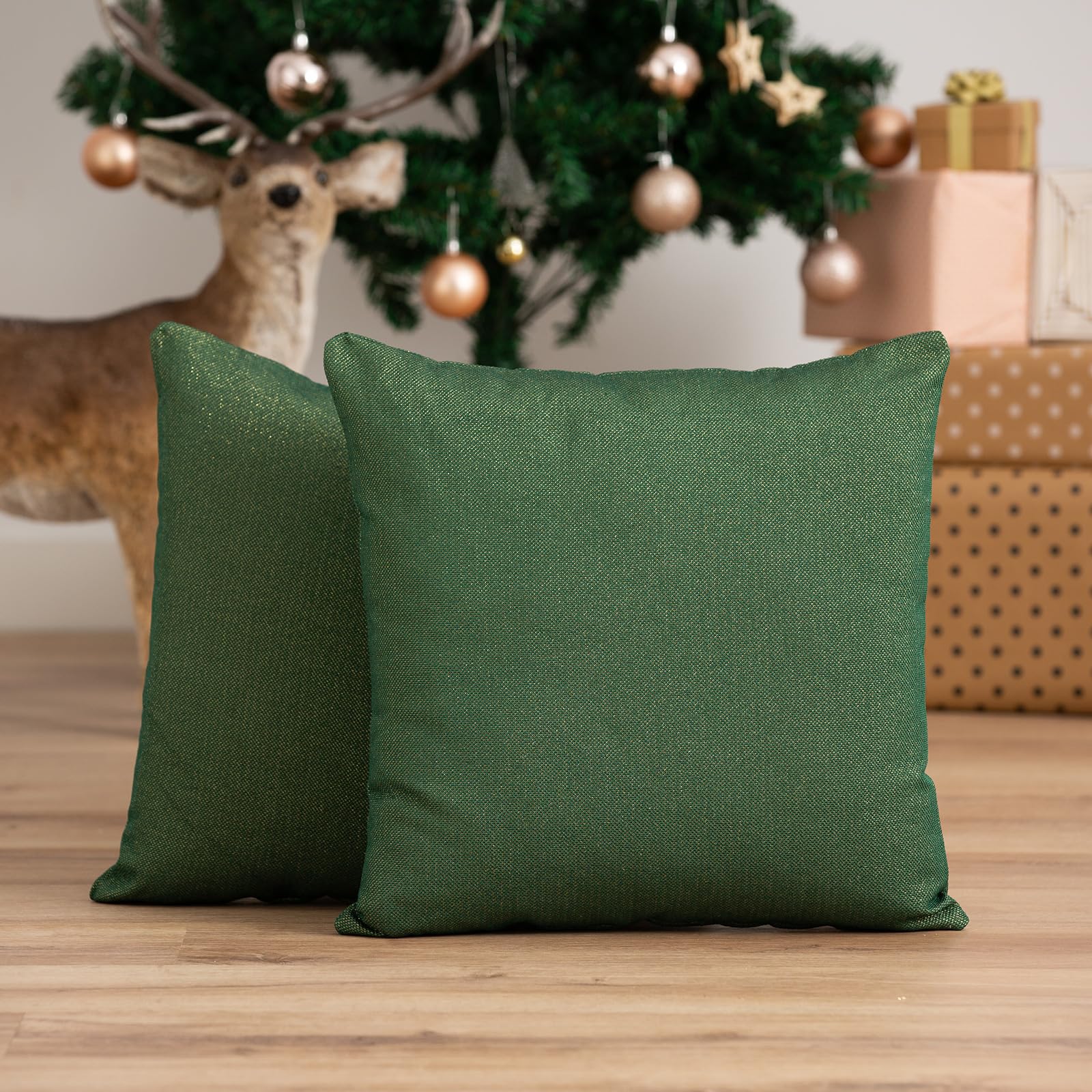 Två gröna kuddfodral framför en julgran med julklappar.