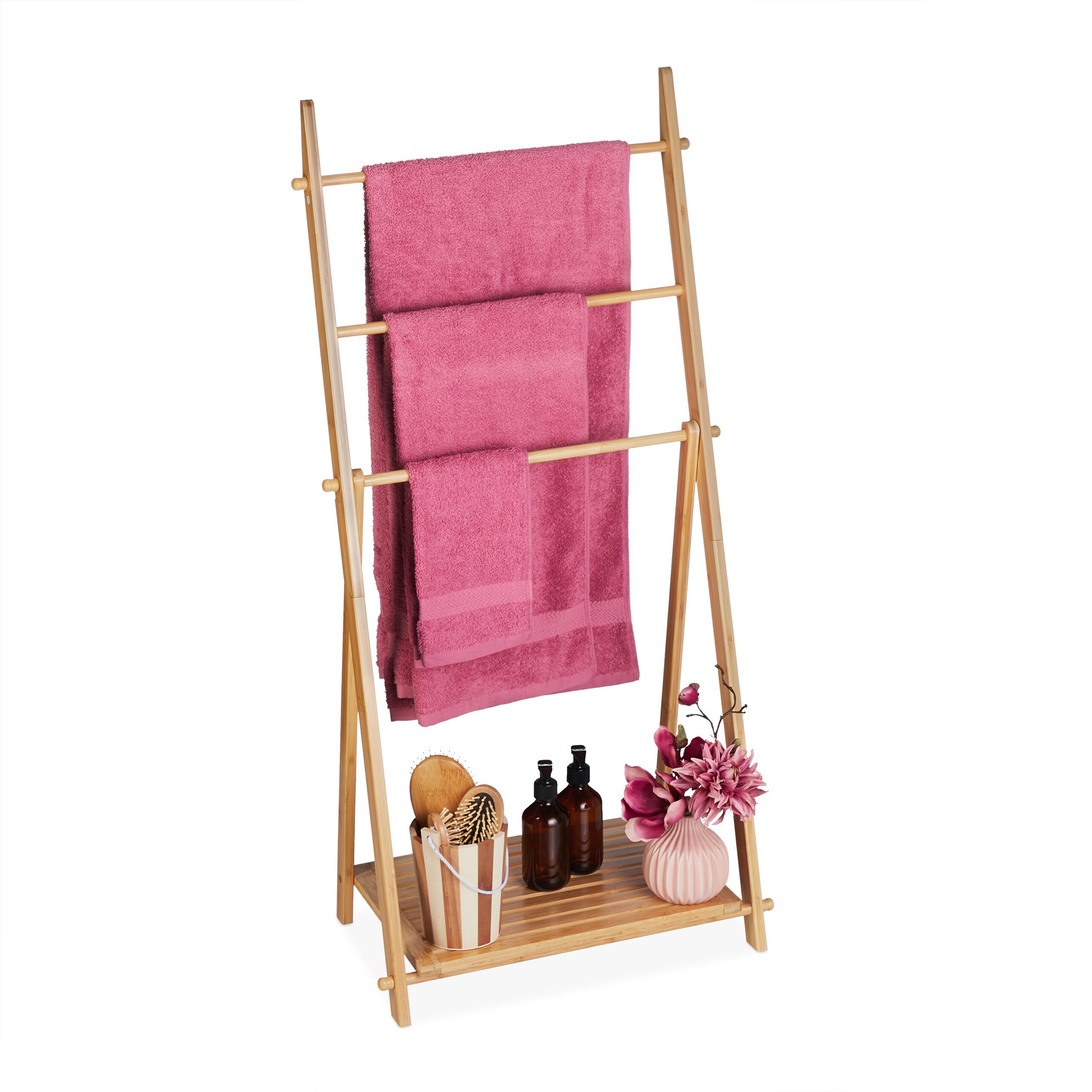 Bambuhanddukshållare med tre rosa handdukar och hylla med badrumstillbehör.