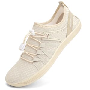 Beige barfotasko med bred tåbox, elastiska snören och ventilerande mönstrad ovandel.