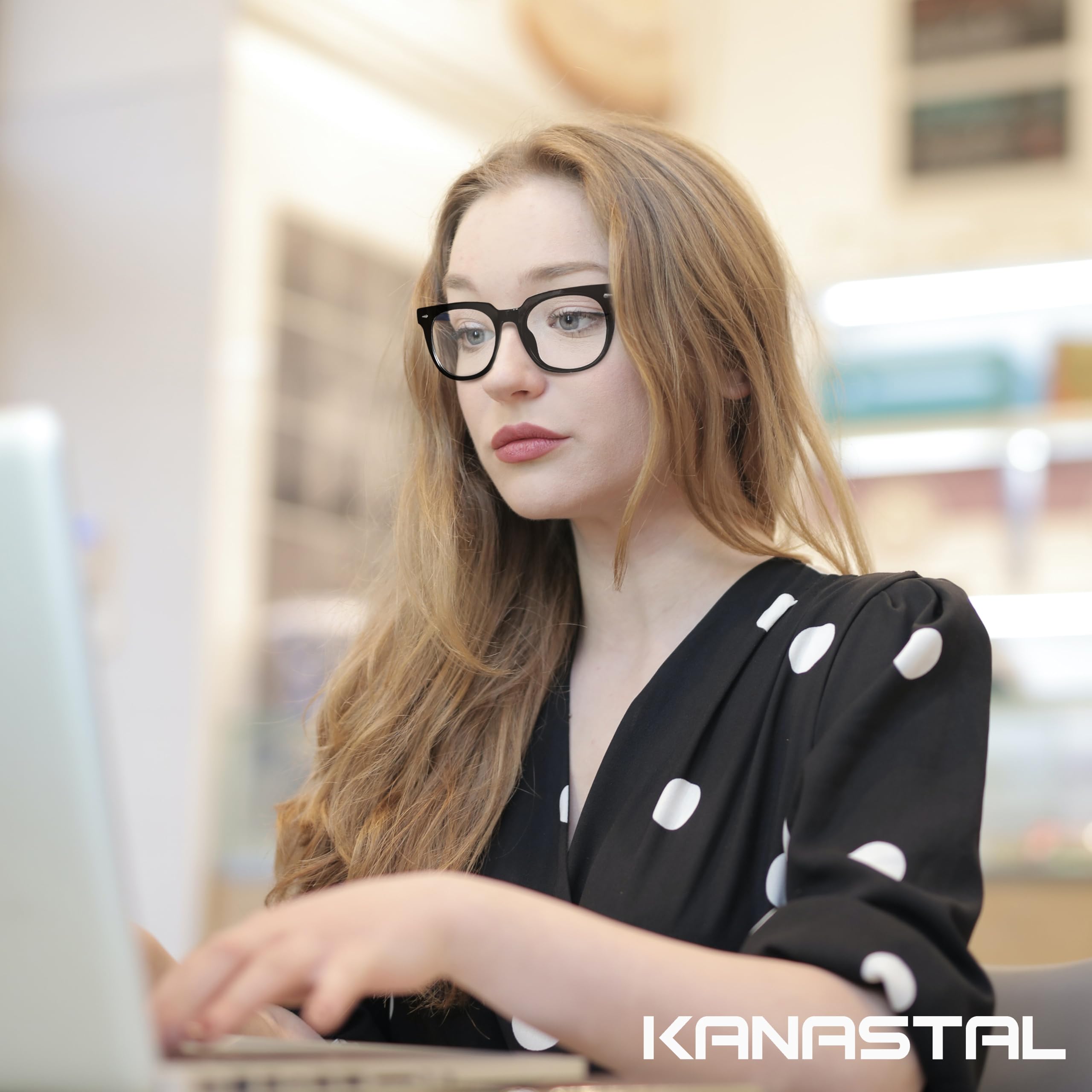 Kvinna med svarta retroglasögon sitter framför en laptop i en ljus butiksmiljö.