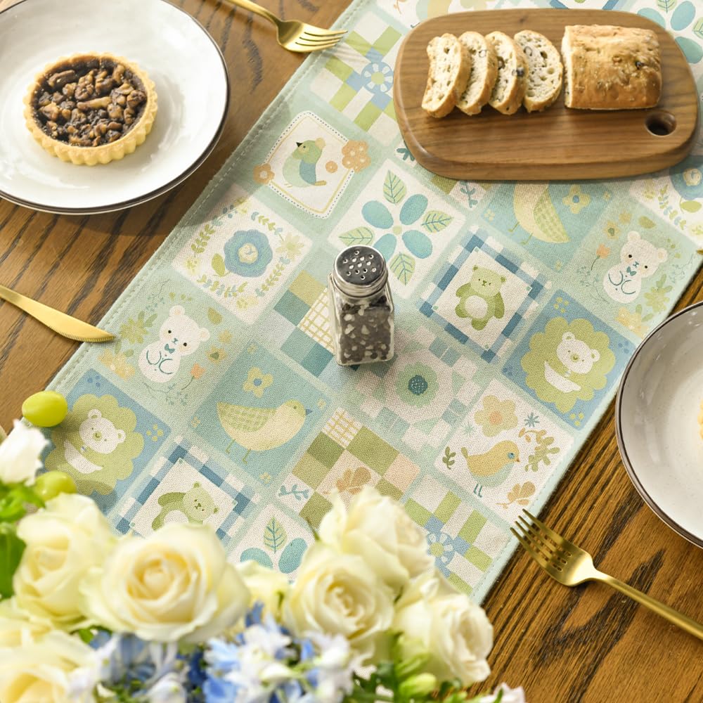 Bordslöpare med nalle- och fågelmotiv dukad med tallrikar, bakverk, skärbräda och blommor.