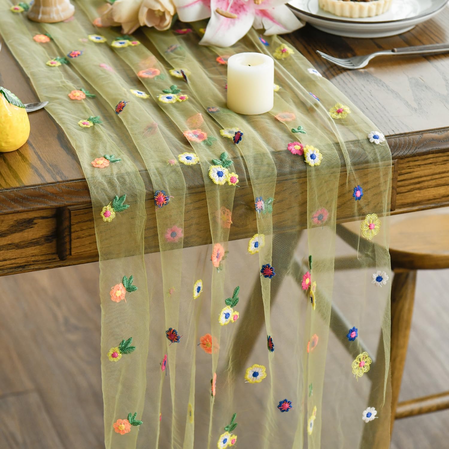 Grön tyllöpare med färgglada broderade blommor på ett dukat träbord.