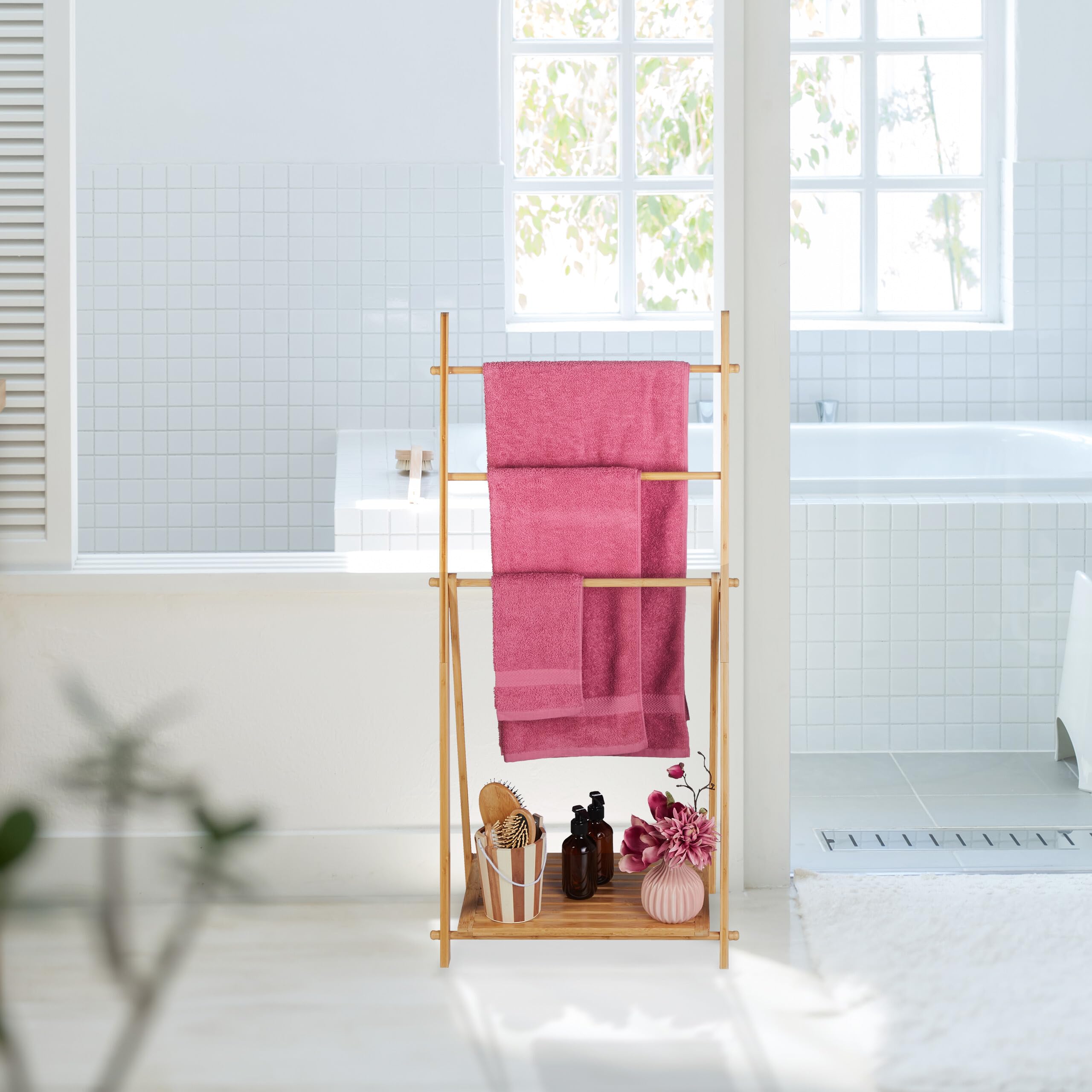 Bambuhanddukshållare med tre stänger, rosa handdukar och hylla med badrumsaccessoarer.