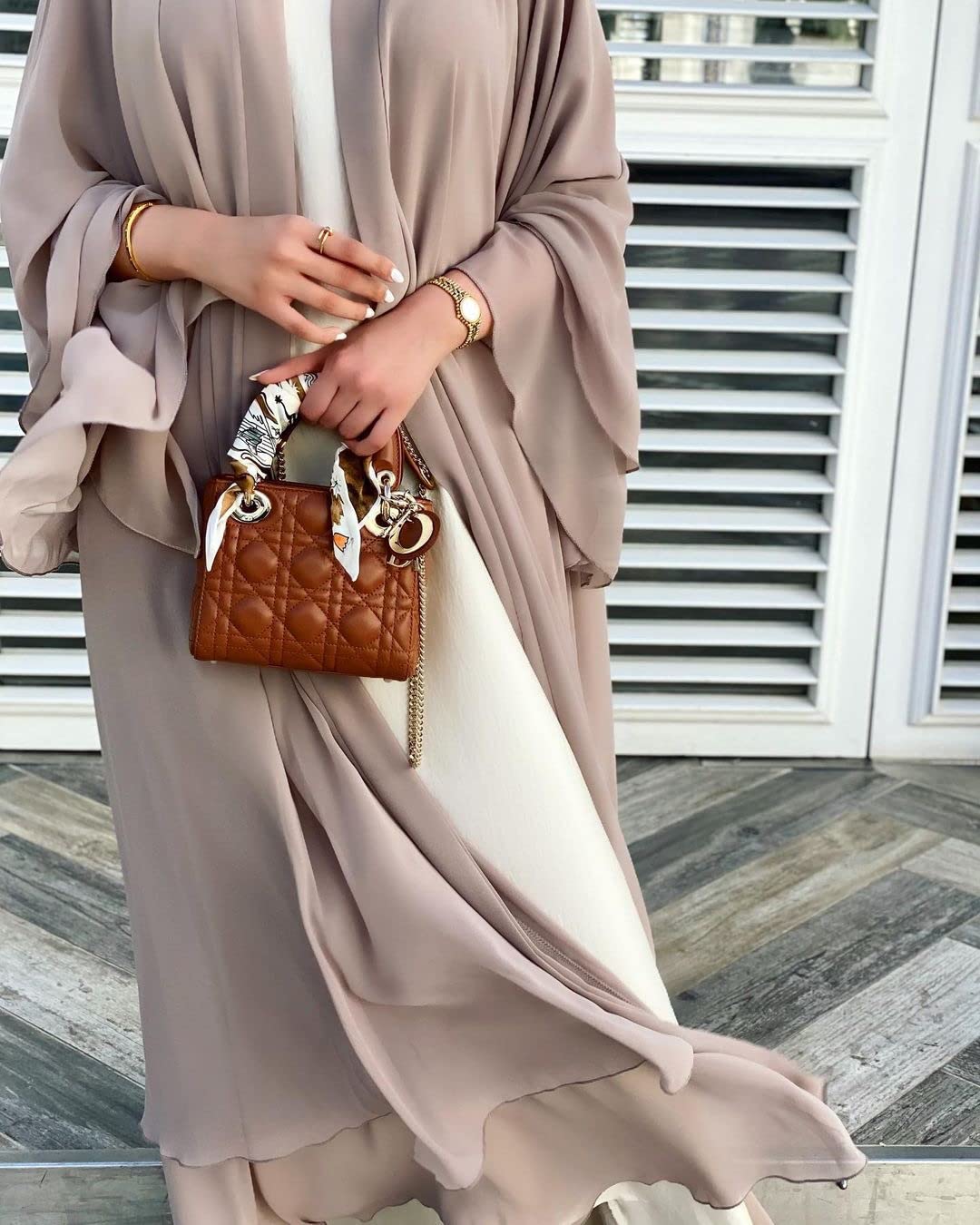 Beige öppen abaya i kaftanstil med vida ärmar och böljande lager över en ljus klänning.